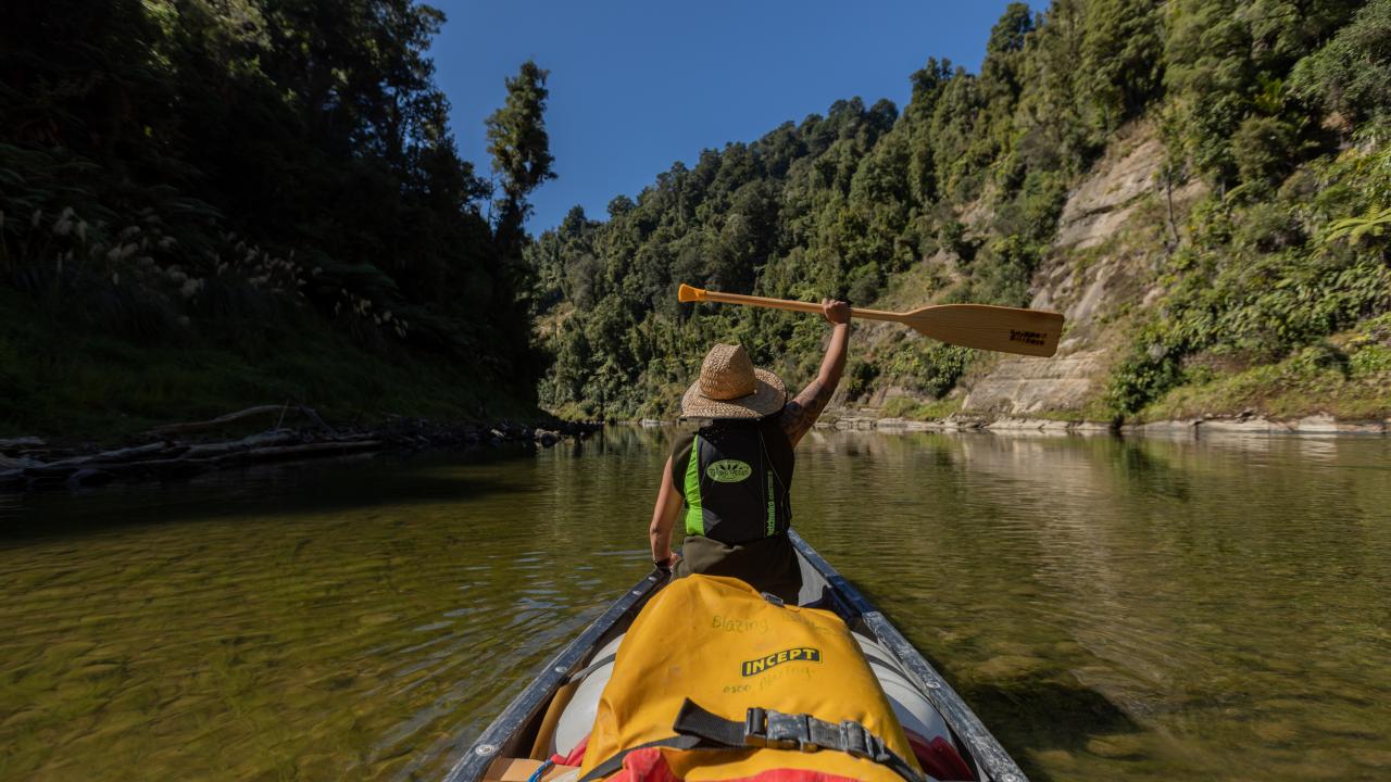 A canoe glides through the shallows as our adventurer holds her paddle aloft