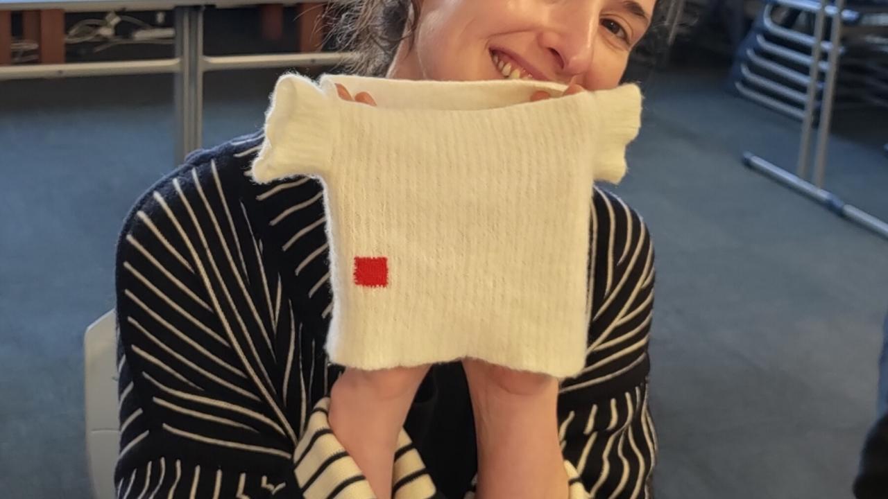 A student holds up their completed creative repaid on a baby shirt at their Visible Mending with a Speedweve Darning Loom Workshop.