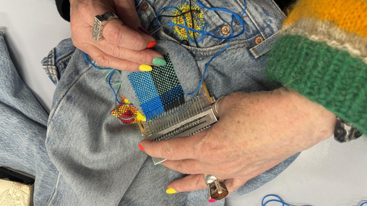 A student repairs a hole in a pair of jeans at their Visible Mending with a Speedweve Darning Loom Workshop.